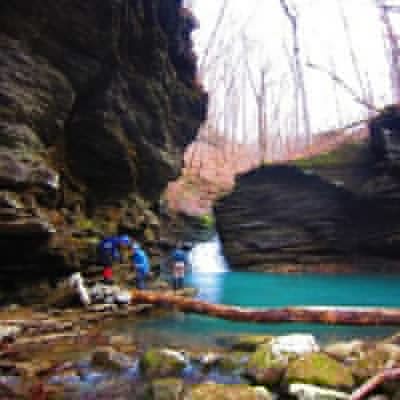 A group of hikers explores a blue pool of water as Bear Creek cascades into it in the Ozark National Forest.
